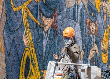 A picture showing the artist Chus at work on "the marching band” mural