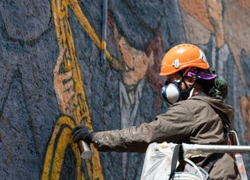 A picture showing the artist Chus at work on "the marching band” mural