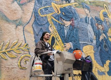 A picture showing the artist Chus at work on "the marching band” mural