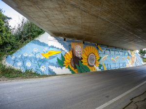 Photo of Chus’s mural under a highway overpass in Italy, depicting the allegory of agriculture