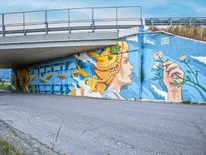 Photo of Chus’s mural under a highway overpass in Italy, depicting the allegory of agriculture